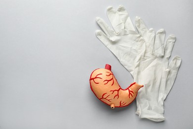 Photo of Anatomical model of stomach and rubber gloves on grey background, flat lay with space for text. Gastroenterology