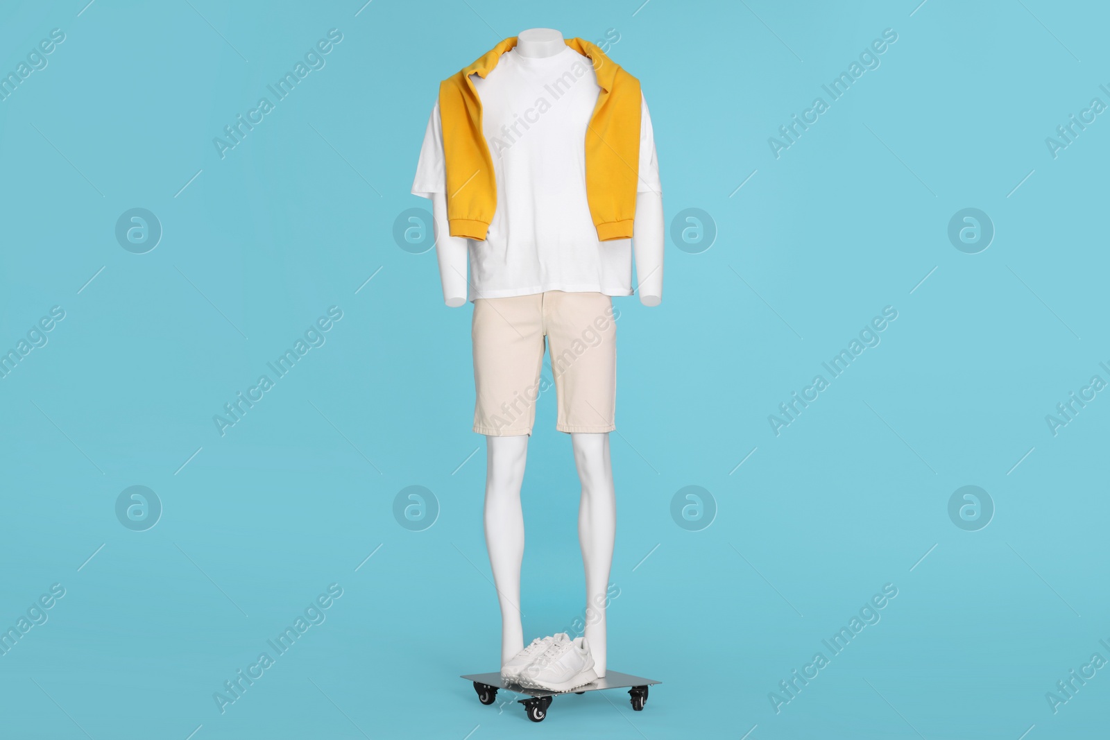 Photo of Male mannequin with sneakers dressed in white t-shirt, stylish shorts and orange sweater on light blue background