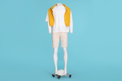 Male mannequin with sneakers dressed in white t-shirt, stylish shorts and orange sweater on light blue background