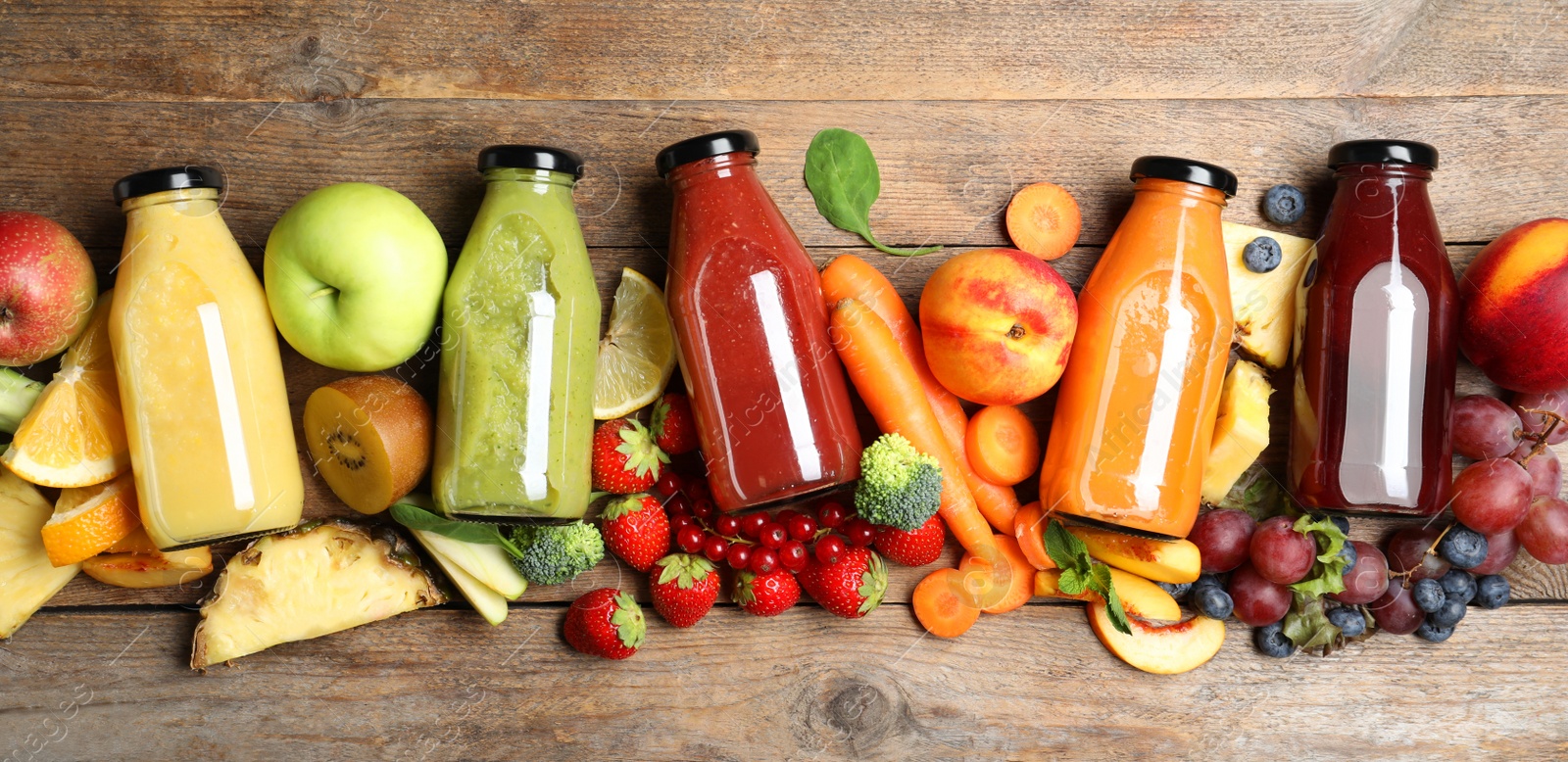 Photo of Bottles of delicious juices and fresh fruits on wooden table, flat lay