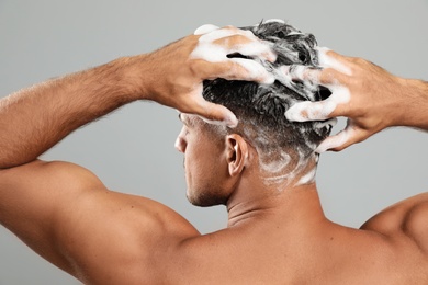 Photo of Handsome man washing hair on grey background, back view
