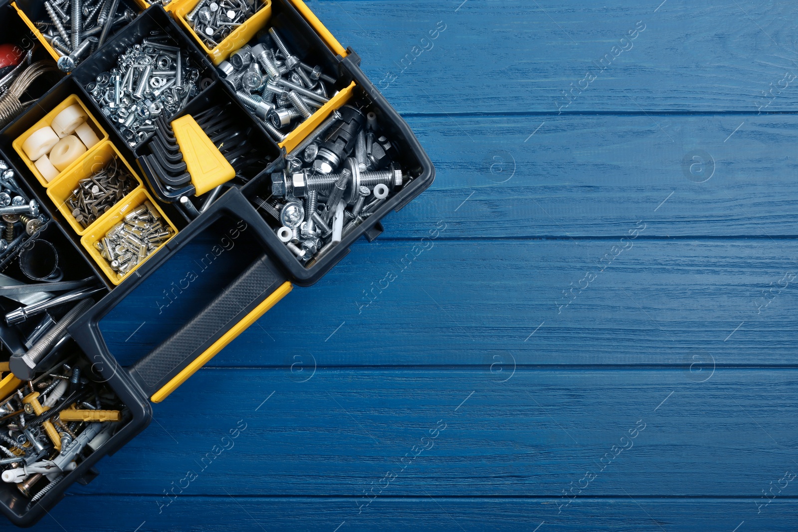 Photo of Plastic box with different furniture fittings and tools on blue wooden table, top view. Space for text