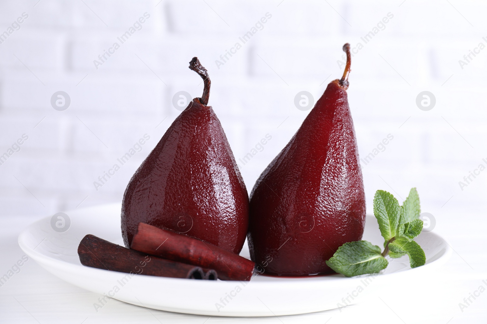 Photo of Tasty red wine poached pears with mint and cinnamon on white wooden table, closeup