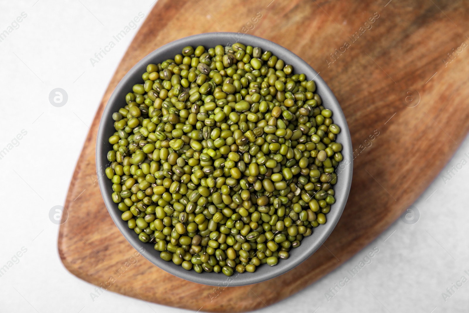 Photo of Bowl with green mung beans and wooden board on white table, top view