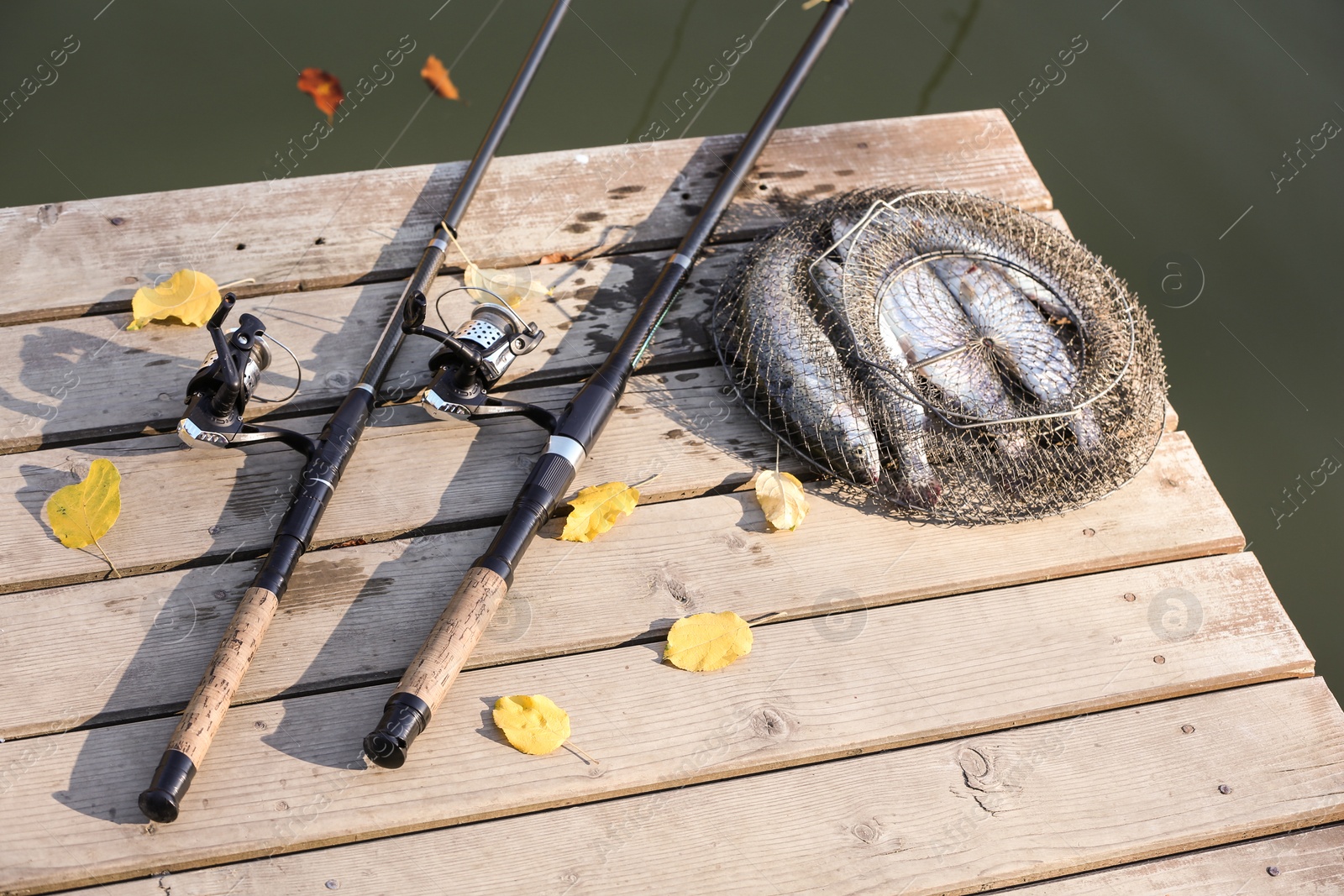 Photo of Fishing rods and fresh fish on wooden pier near pond