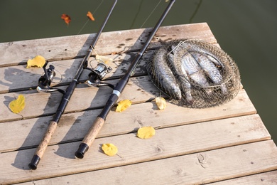 Fishing rods and fresh fish on wooden pier near pond