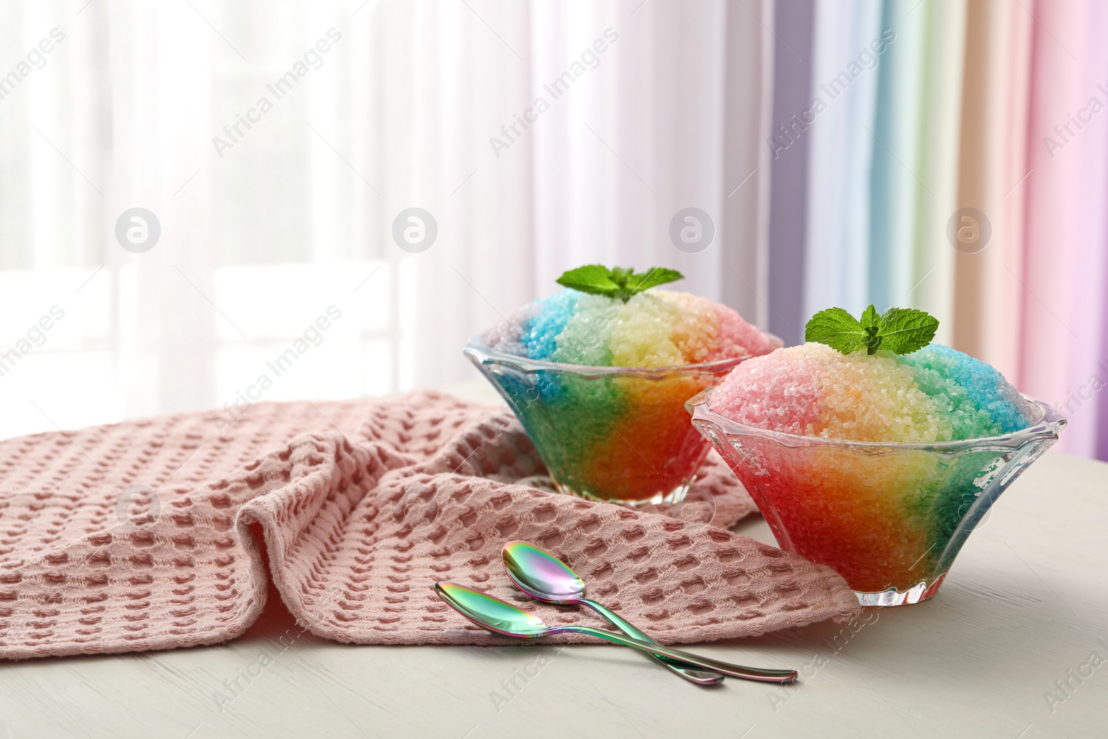 Photo of Rainbow shaving ice in glass dessert bowls and spoons on wooden table indoors