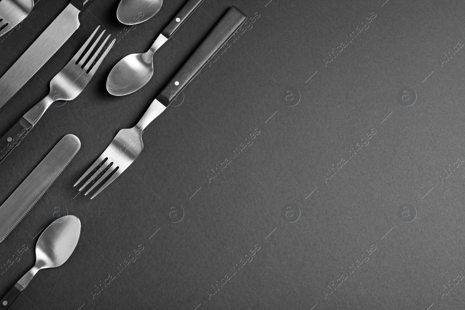 Photo of Set of new metal cutlery on black background, flat lay with space for text