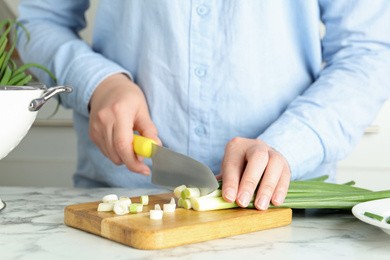 Photo of Woman cutting green spring onions on wooden board at white marble table, closeup