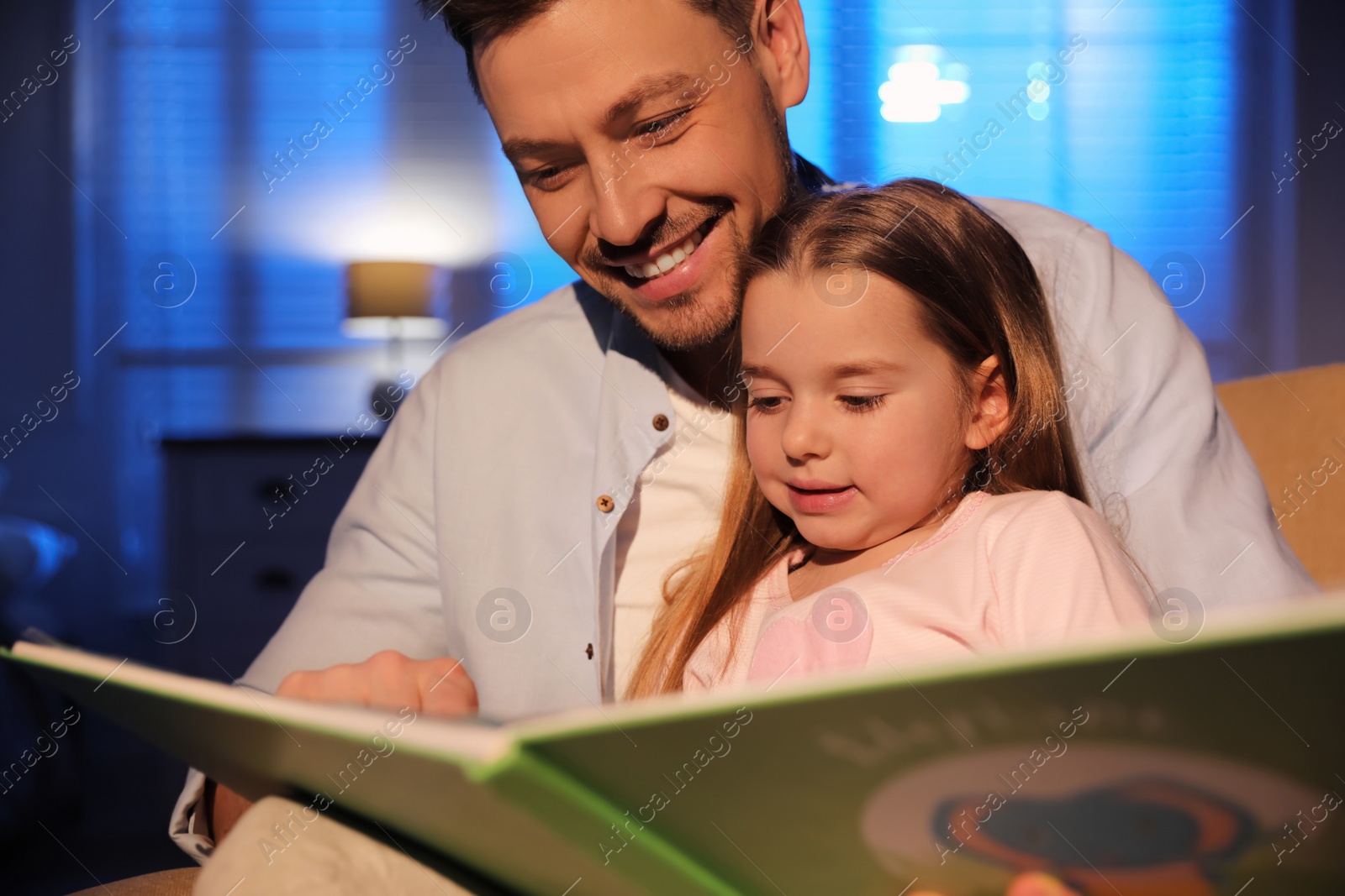 Photo of Father reading bedtime story to his daughter at home