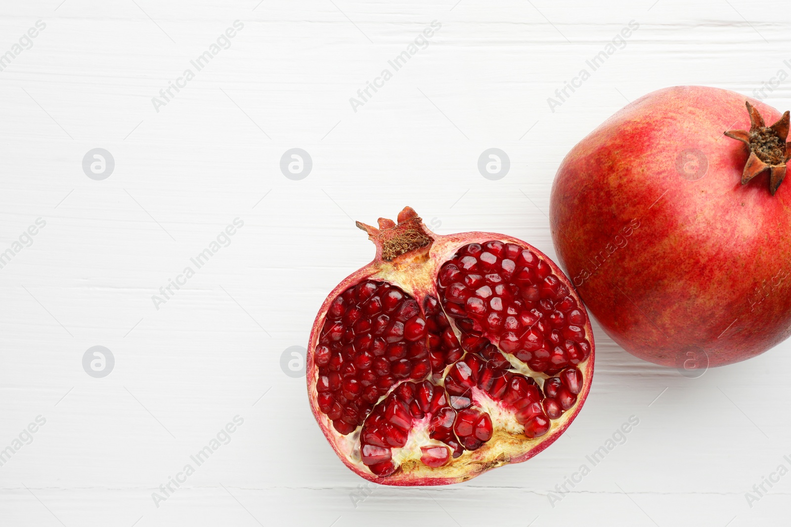 Photo of Fresh pomegranates on white wooden table, top view. Space for text