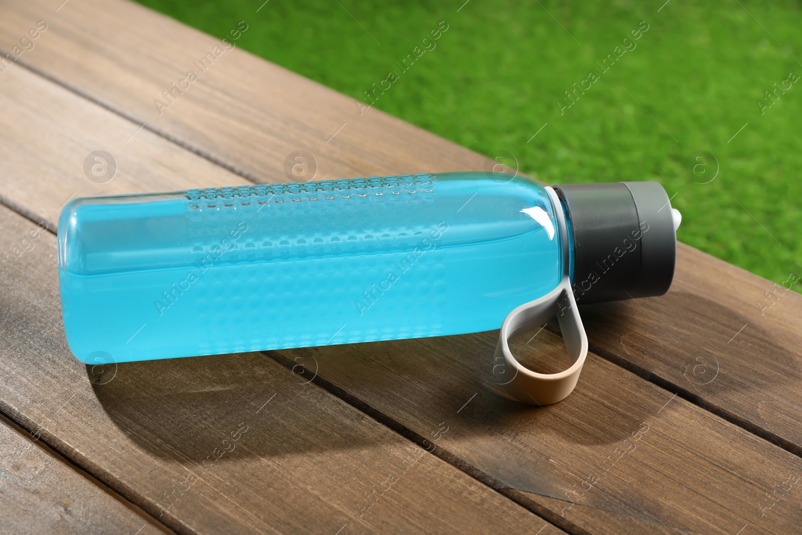 Photo of Light blue drink in bottle on wooden table outdoors