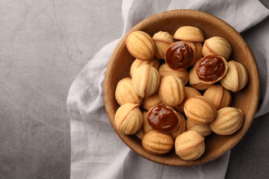 Photo of Delicious nut shaped cookies with boiled condensed milk in wooden bowl on gray textured table, top view