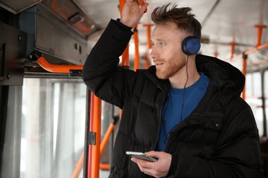 Photo of Young man listening to music with headphones in public transport. Space for text