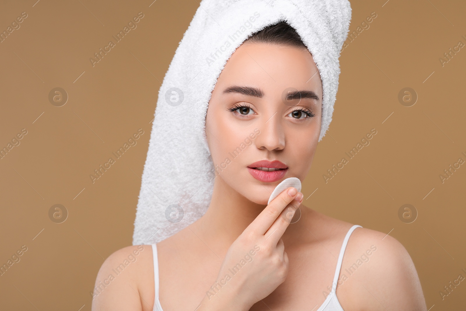 Photo of Beautiful woman in terry towel removing makeup with cotton pad on beige background