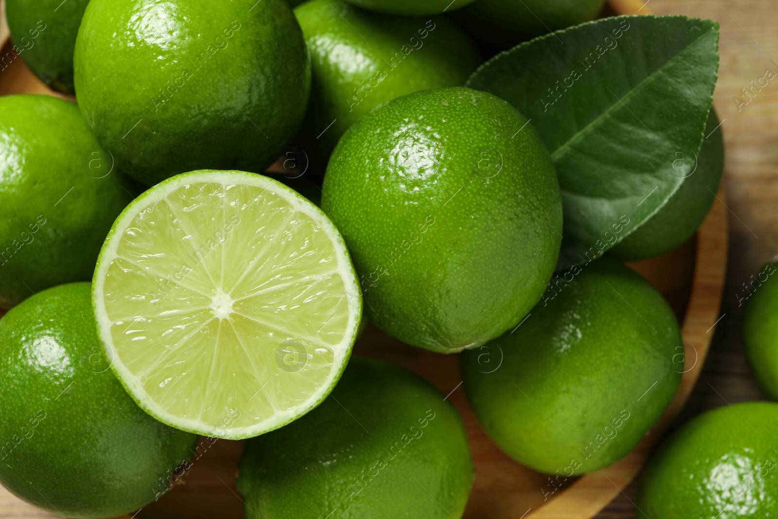 Photo of Fresh ripe limes and green leaf on table, closeup