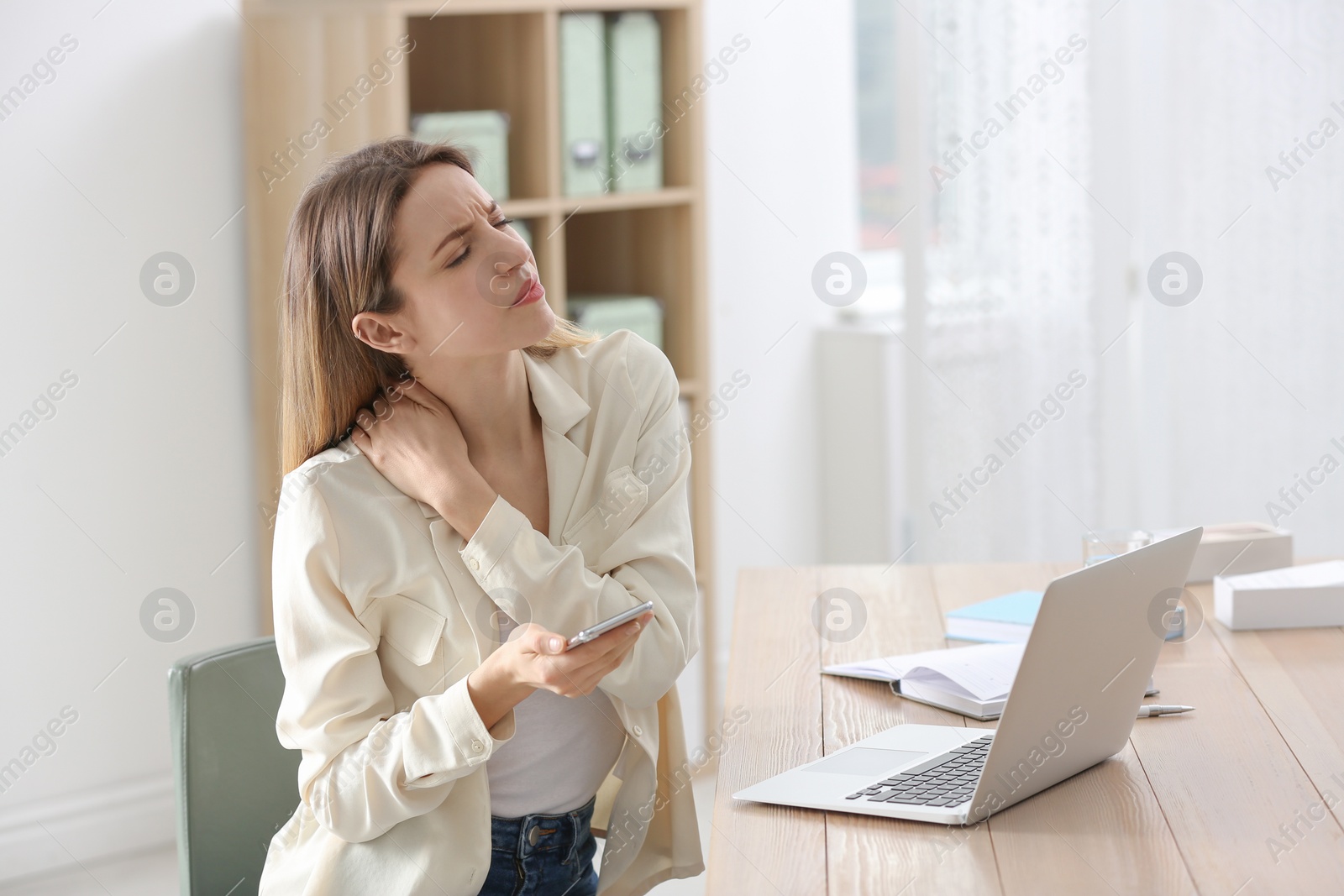 Photo of Woman with smartphone suffering from neck pain in office. Symptom of bad posture