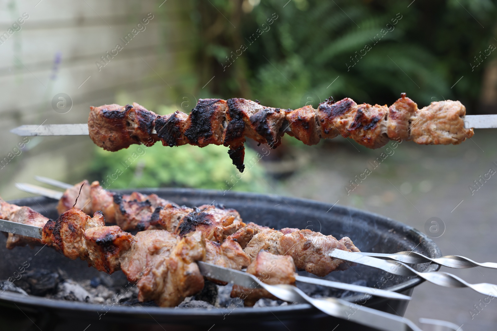 Photo of Cooking delicious kebab on metal skewers outdoors