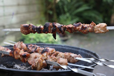 Photo of Cooking delicious kebab on metal skewers outdoors