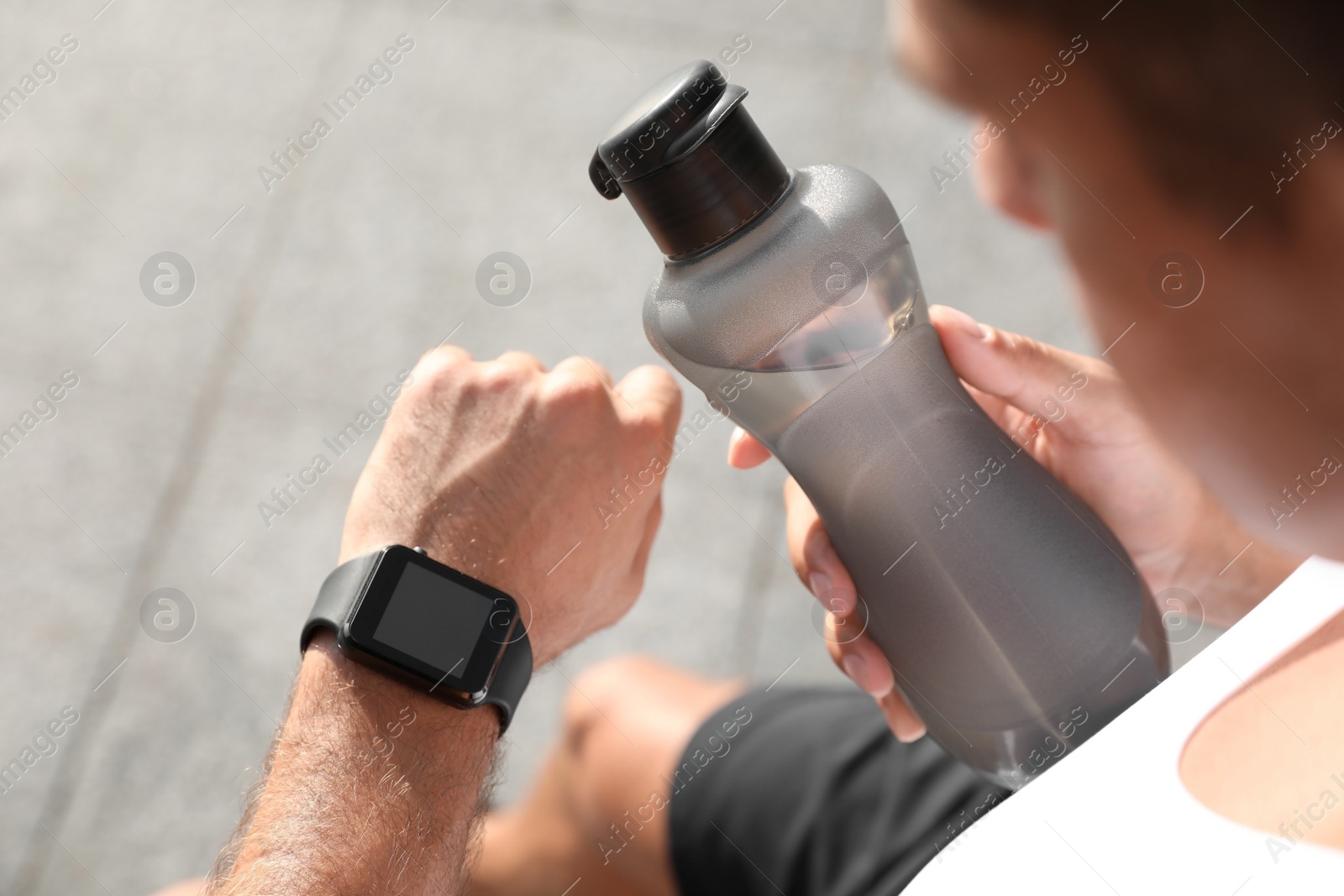 Photo of Man with bottle of water checking fitness tracker after training outdoors, closeup
