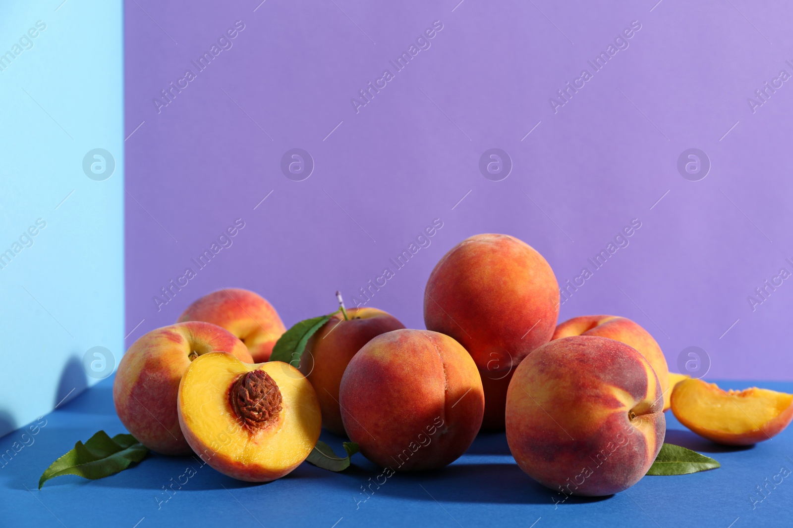 Photo of Fresh ripe peaches and green leaves on color background