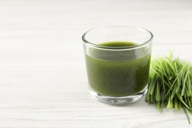 Photo of Wheat grass drink in glass and fresh sprouts on white wooden table, closeup. Space for text