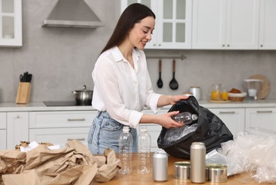 Photo of Smiling woman separating garbage at table in kitchen
