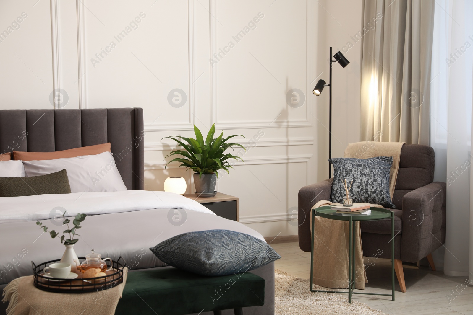 Photo of Stylish bedroom interior with large comfortable bed, armchair and ottoman