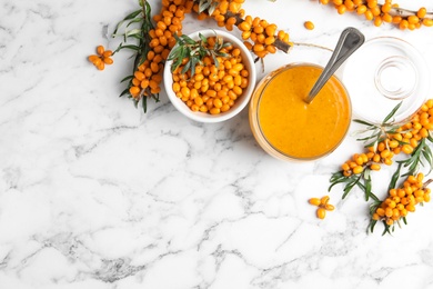 Delicious sea buckthorn jam and fresh berries on white marble table, flat lay. Space for text