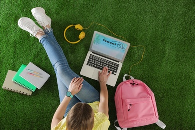 Photo of Woman and laptop with open travel blogger site on artificial grass, top view