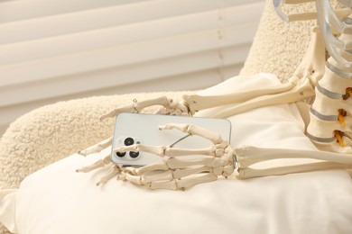 Waiting concept. Human skeleton with smartphone sitting in armchair indoors, closeup