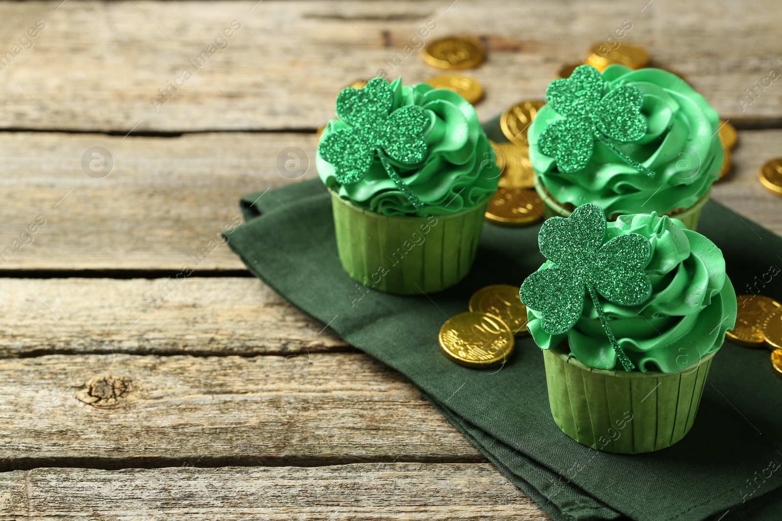 Photo of St. Patrick's day party. Tasty cupcakes with clover leaf toppers and green cream on wooden table, closeup. Space for text