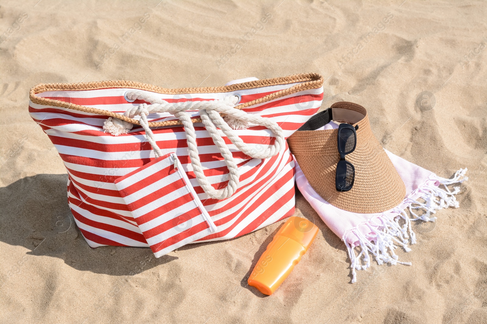 Photo of Stylish striped bag with beach accessories on sand