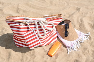 Stylish striped bag with beach accessories on sand