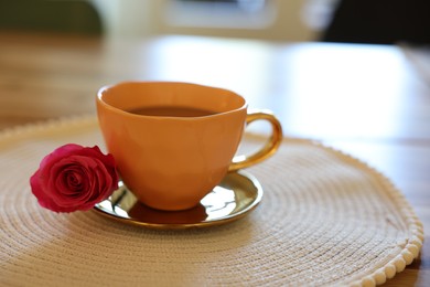 Photo of Cup of hot drink and red rose on table indoors, closeup. Space for text