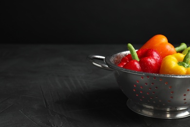 Colander with wet ripe bell peppers on grey table against black background, space for text