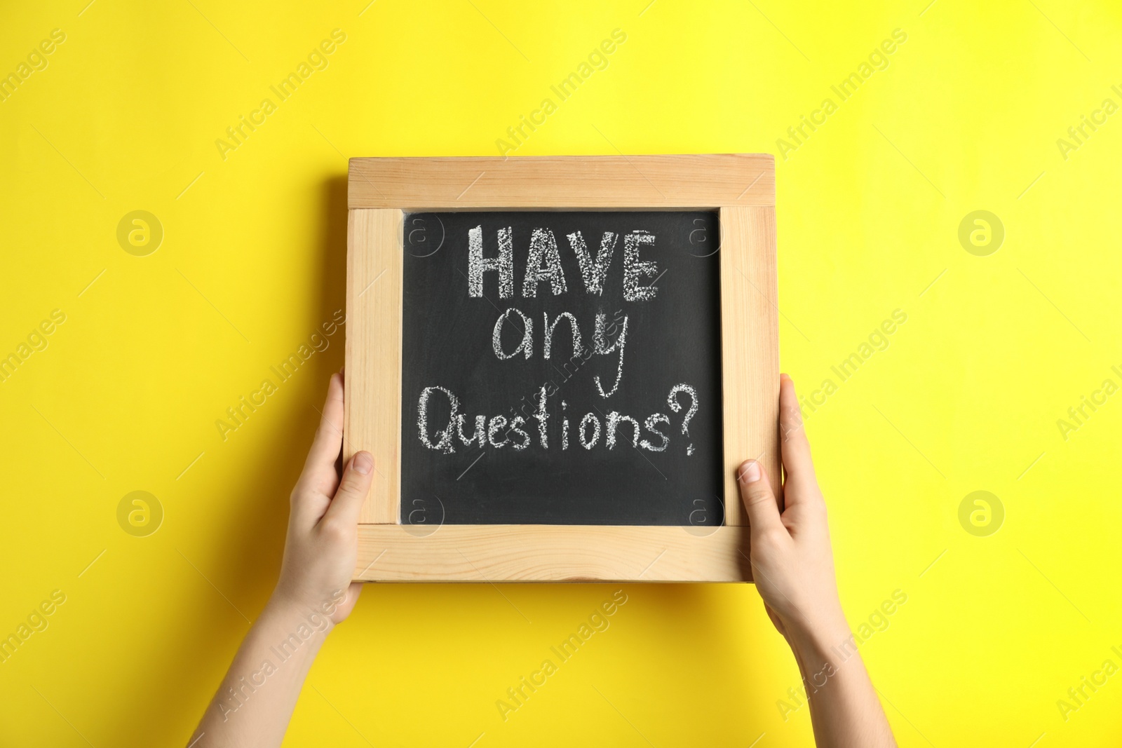 Photo of Woman holding blackboard with phrase HAVE ANY QUESTIONS on yellow background, closeup