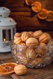 Photo of Bowl of delicious nut shaped cookies and dried orange slices on wooden table, closeup