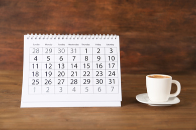 Photo of Calendar and cup of coffee on wooden table