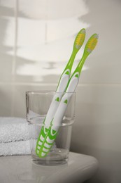 Light green toothbrushes in glass holder on washbasin