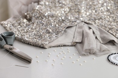 Photo of Silver fabric with paillettes, beads and scissors on white table