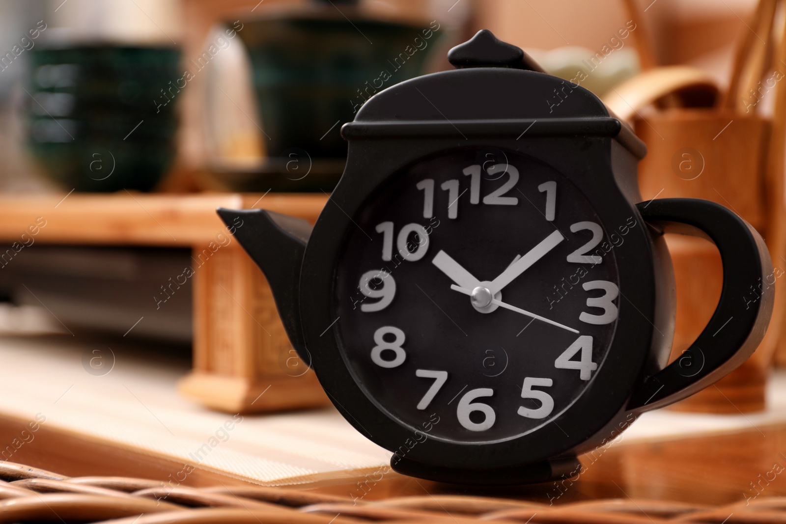 Photo of Teapot shaped clock on wooden stand indoors, closeup