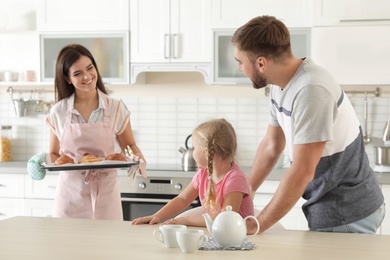 Photo of Young beautiful woman treating her family with freshly oven baked buns in kitchen