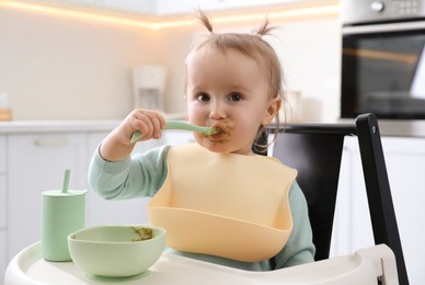 Photo of Cute little baby eating food in high chair at kitchen