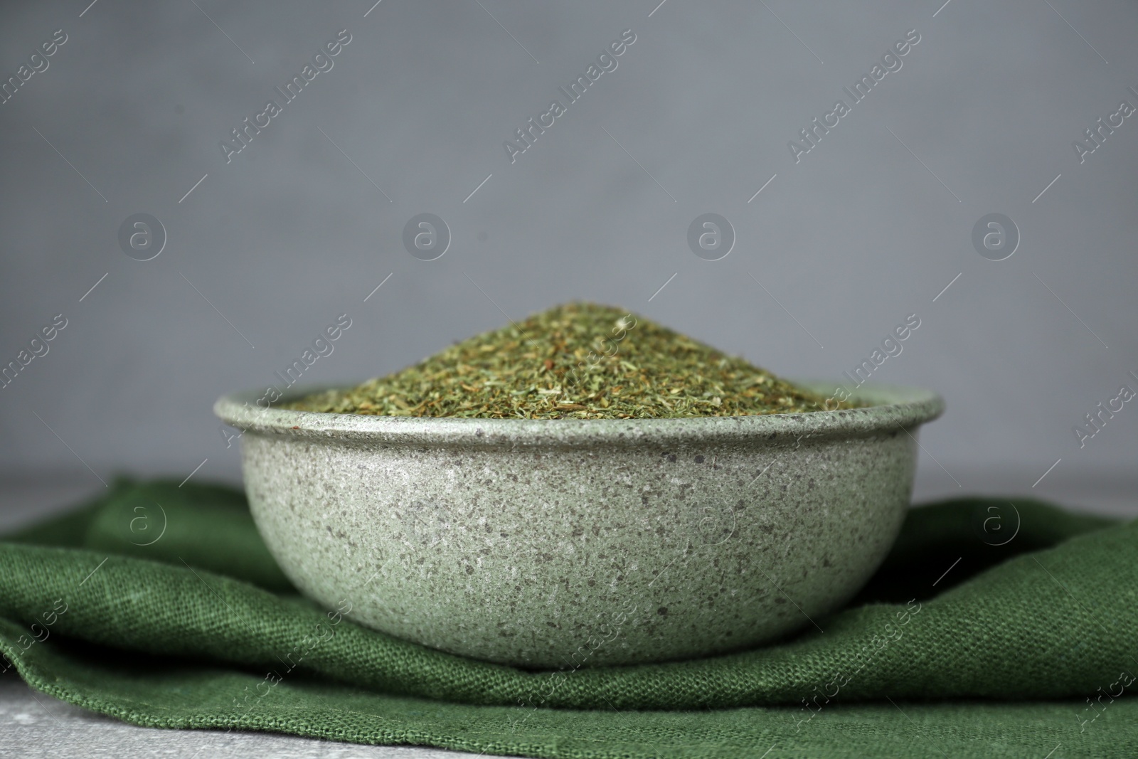 Photo of Dried dill in bowl and green towel on table against grey background, closeup