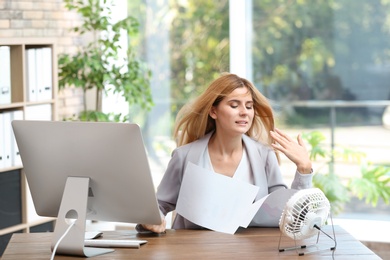 Businesswoman suffering from heat in front of small fan at workplace