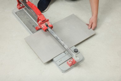 Photo of Worker using manual tile cutter on floor, closeup