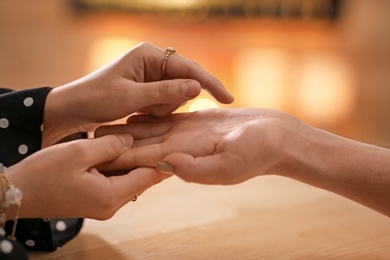 Chiromancer reading lines on woman's palm at table, closeup