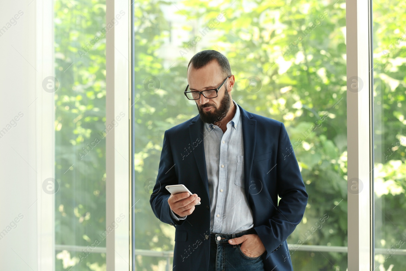 Photo of Portrait of handsome mature man in elegant suit with mobile phone near window