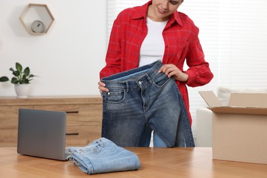 Young woman with just unpacked new jeans and laptop on wooden table indoors, closeup. Online shopping